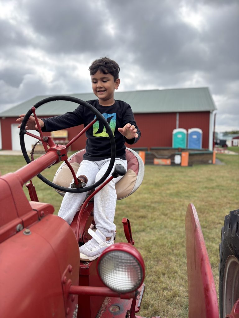 Child sitting in red tractor on farm.