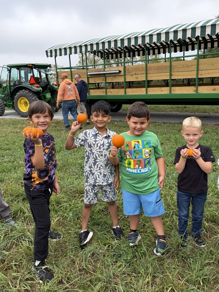 Three children holding pumpkins in front of a trailer, posing for a picture.