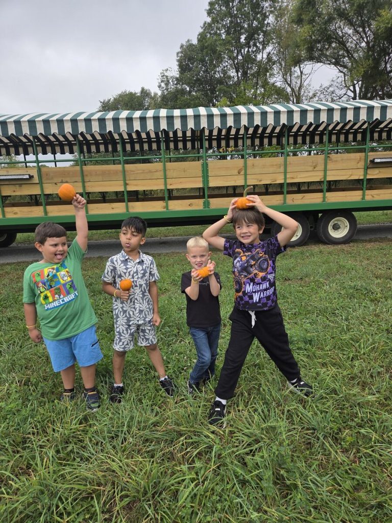 Four children posing in front of a trailer filled with oranges.