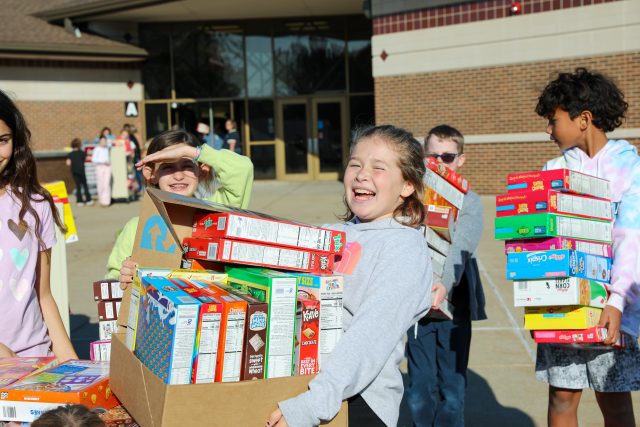 Girl poses for photo holding many cereal boxes.