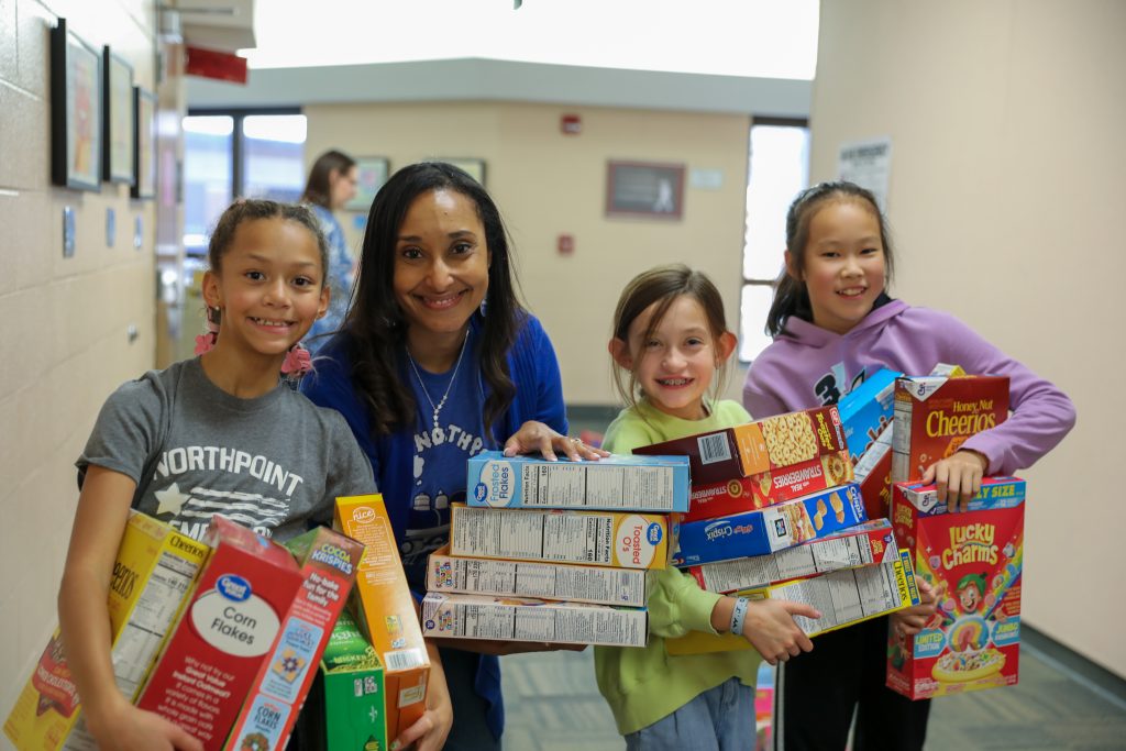 Students and principal pose with cereal boxes for a picture.