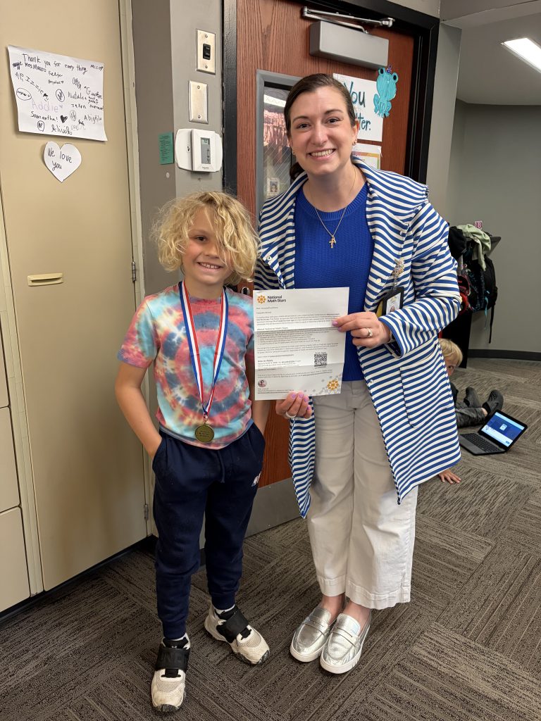 Woman holding a medal with a boy beside her. They are in an office setting.